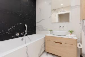 ein Badezimmer mit einem Waschbecken, einer Badewanne und einem Spiegel in der Unterkunft Deluxe Apartment Wronia 45 with AC, Parking & Balcony by Renters Prestige in Warschau