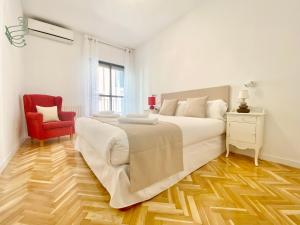 a white bedroom with a large bed and a red chair at Charming Gran Vía V - Largas Estancias in Madrid