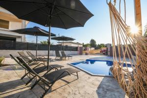 un grupo de sillas y sombrillas junto a una piscina en Nektarios & Eftychia Suites en Ambelókipoi