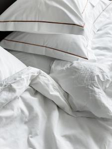 1 cama no hecha con sábanas y almohadas blancas en Amberton Green SPA Druskininkai en Druskininkai