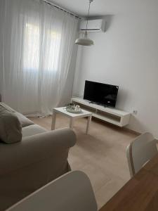 ein Wohnzimmer mit einem Sofa, einem TV und einem Tisch in der Unterkunft SHERRY SUITES VIII Apartamentos PARKING GRATUITO in Jerez de la Frontera