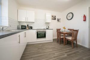cocina con armarios blancos, mesa y reloj en Tranmere House Workstays UK Best Rates Direct, en Middlesbrough