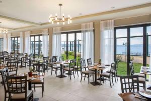 uma sala de jantar com mesas, cadeiras e janelas em Ramada by Wyndham , Athens Club Attica Riviera em Mati
