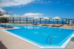 une grande piscine bleue avec des chaises et des parasols dans l'établissement Ramada by Wyndham , Athens Club Attica Riviera, à Mati
