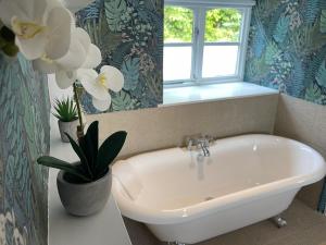 baño con bañera blanca, ventana y flores en Snowdonia Holiday Cottages, en Conwy