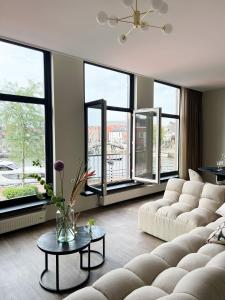 een woonkamer met een bank, een tafel en ramen bij Reen Luxury Stays - Waterpoort -2 bedrooms, 4 pers in Sneek