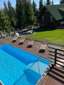 einen Pool mit einer Terrasse und Stühlen sowie ein Haus in der Unterkunft Transylvania Villa & Spa in Muntele Băişorii