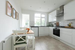 uma cozinha com armários brancos e uma mesa e cadeiras em Spacious 3BR House, 8 min Kensal Green, NW London em Londres