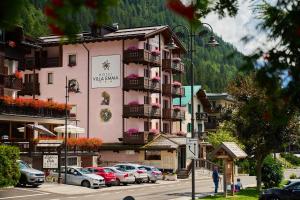 a large pink building with cars parked in a parking lot at Hotel Villa Emma in Madonna di Campiglio