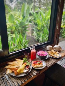 a table with plates of food on a table with a window at Kabinji Bali in Tampaksiring