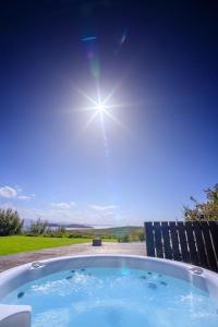 bañera de hidromasaje con el sol en el cielo en Locholly Lodge, en Achiltibuie