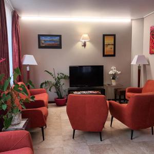 une salle d'attente avec des chaises rouges et une télévision à écran plat dans l'établissement Hotel Capitole, à Beausoleil