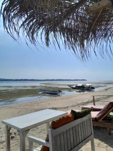a table and chairs on a beach with the ocean at Why Not Bar And Bungalows in Pawenang +5 photos