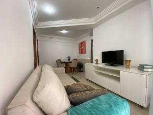 uma sala de estar com um sofá branco e uma televisão em PRAIA DA COSTA - 02 QUARTOS - SOL E MAR em Vila Velha