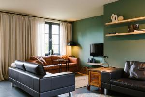sala de estar con muebles de cuero y TV en Hoeve de Reetjens - La Gouvernante en Bilzen