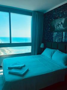 a bedroom with a blue bed with a large window at Sea Breeze Studios in Netanya