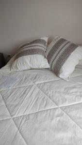 Una cama blanca con dos almohadas encima. en Duplex Pinamar norte frente al bosque en Pinamar