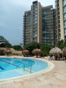una piscina con sombrillas de paja, sillas y edificios en Beautiful Beach Apartment in Zazue, en Santa Marta