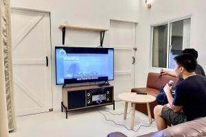 two men sitting in a living room playing a video game at เดอะ ชะอม The ChaOm in Ban Cha-om