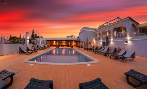 a pool with chairs and a sunset in the background at Villa Welwitshia in Carvoeiro