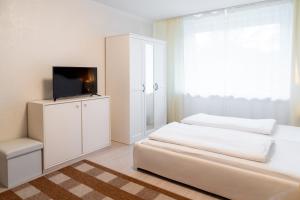 a white bedroom with a bed and a tv on a cabinet at Hotel zum Hahn in Garbsen
