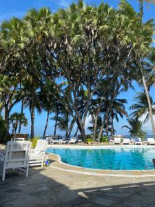 a swimming pool with chairs and palm trees at Kilili Baharini Resort & Spa in Malindi