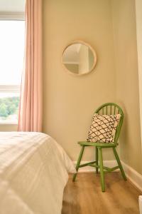 a green chair in a bedroom with a mirror at Wood End View - Traditional Top-and-Bottom House in Hebden Bridge