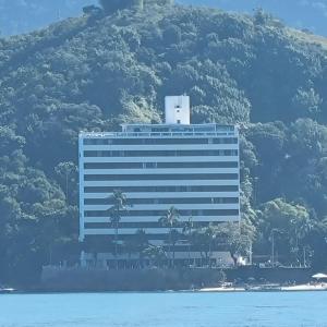 a large building with palm trees in front of a mountain at Apartamento Pé na Areia in Caraguatatuba