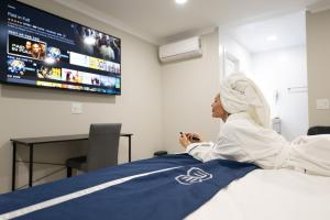 a woman laying on a bed watching a tv at Omeo Suites in Alhambra