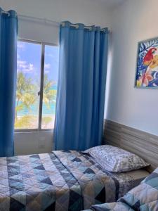 a bedroom with a bed and a window with blue curtains at Apart Hotel Marinas Tamandaré in Tamandaré