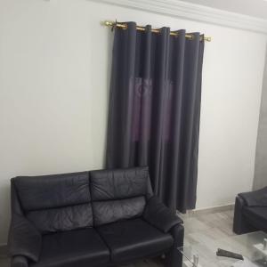un sofá negro sentado en una sala de estar junto a una cortina en RÉSIDENCE 2k en Yaundé