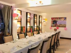 Maison Arnica Hotel & Restaurant في بنوم بنه: طاولة طويلة مع طاولات بيضاء وكراسي في غرفة