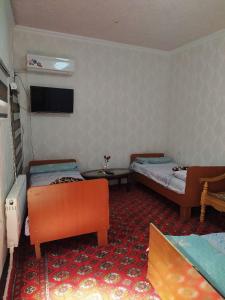 a room with two beds and a tv on the wall at Masturabonu Ravshan in Bukhara