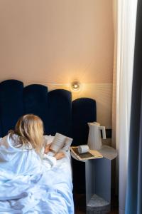 Una donna sdraiata a letto che legge un libro accanto a un tavolo di Condominio Monti Boutique Hotel a Roma