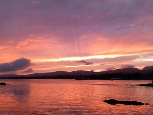 una puesta de sol sobre un cuerpo de agua con montañas en Watersedge Seaviews en Kenmare