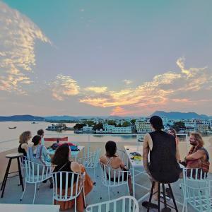 een groep mensen die in stoelen zitten te kijken naar de zonsondergang bij Hostel Mantra in Udaipur