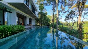 an infinity pool in front of a house with trees at Maxwell Villa Bali in Tabanan