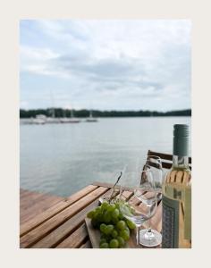 een fles wijn en druiven op een tafel naast het water bij Port Sztynort in Węgorzewo