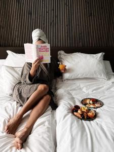 a person laying on a bed reading a book with two plates of food at Mana Sleep & Spa in Druskininkai