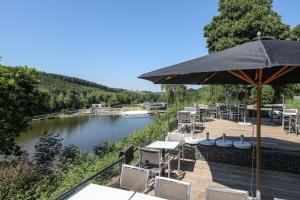 een patio met tafels en een parasol naast een rivier bij Hotel Bô Rivage -- Eden-Ardenne in Neufchâteau