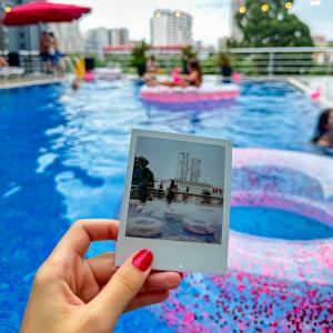 a person holding a picture in front of a swimming pool at New Wave Hotel in Batumi
