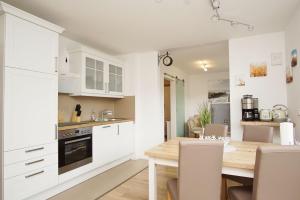 a kitchen and dining room with white cabinets and a wooden table at schöne 2-Raum-Wohnung mit Balkon, gratis Nutzung vom AHOI Erlebnisbad und Sauna in Sellin - Villa Jolie FeWo 09 in Ostseebad Sellin