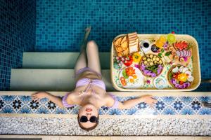 une femme qui se couche dans une piscine avec un plateau de nourriture dans l'établissement Lantana Boutique Hoi An Hotel, à Hội An