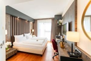 a hotel room with a bed and a desk and a mirror at PLAZA Premium Karlsruhe in Karlsruhe