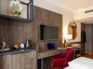 a hotel room with a desk and a tv on a wall at PLAZA Premium Karlsruhe in Karlsruhe