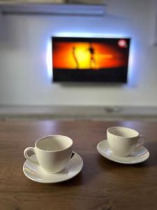two white cups and saucers on a table with a tv at Cozy and quiet apartment in Arad +1 photo