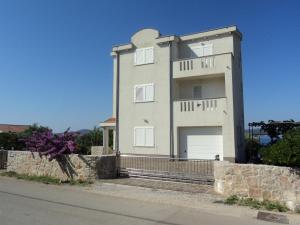 a large white house with a stone wall at Apartments Delfini in Sveti Filip i Jakov