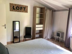 1 dormitorio con cama, silla y espejo en La petite maison au chêne en Belin-Beliet