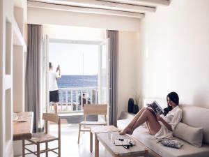 a woman sitting on a couch reading a book in a living room at Bill & Coo Coast Suites -The Leading Hotels of the World in Agios Ioannis Mykonos