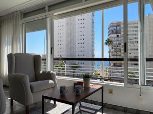 uma sala de estar com uma cadeira, uma mesa e janelas amplas em Apartamento a un minuto de la playa de Levante em Benidorm